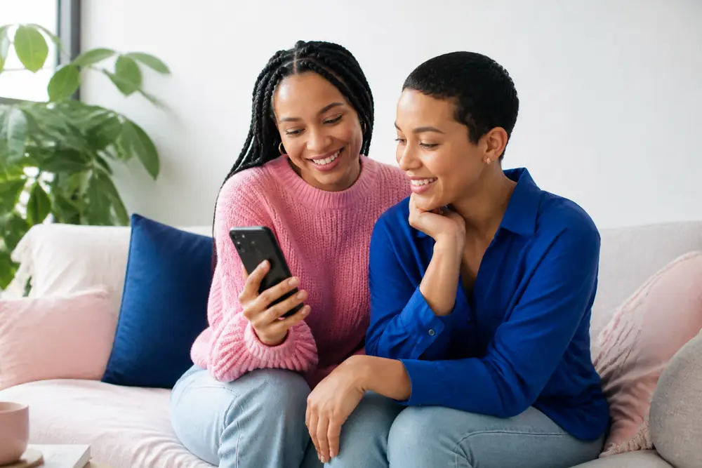 Two friends on a couch smiling at something on a phone
